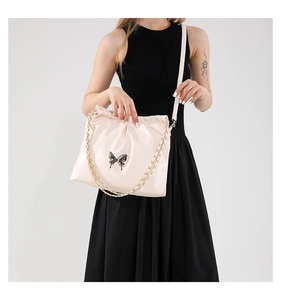 Close-up of beige PU leather bag with silver butterfly charm and chain strap detail