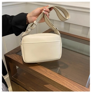 Detail of a beige PU leather camera bag featuring a wide woven retro shoulder strap