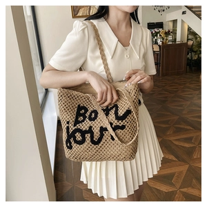 Detailed macro view of a beige woven tote bag featuring black Bon jour embroidery detail