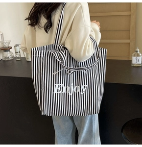 Detail shot of a black and white striped canvas tote bag with Enjoy print on a model