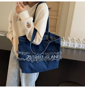 Détail du sac cabas en jean bleu avec broderie blanche et bords à franges effilochés