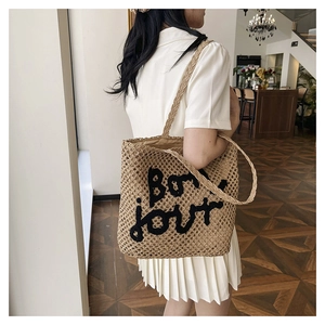 Close-up of beige woven straw tote bag featuring black Bonjour embroidery and handle detail