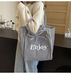 Close-up of striped canvas tote bag with Enjoy typography on a model in a cafe setting