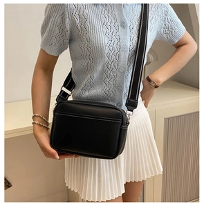 Detail of black PU leather crossbody bag featuring white stitching and striped strap