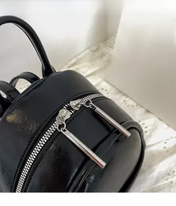 Detail view of smooth black PU leather backpack showing silver dual zippers and handle