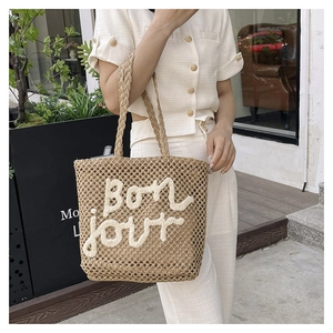 Detail of woven straw tote bag with white 3D Bonjour embroidery for a summer beach look