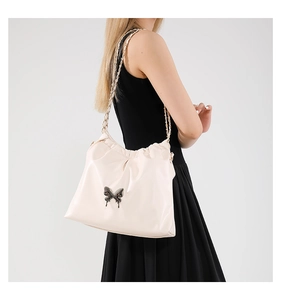 Close-up of cream PU crossbody bag featuring metal butterfly charm and woven chain strap