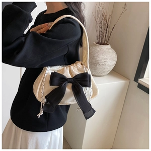 Close-up of cream corduroy shoulder bag featuring a large decorative black bow detail