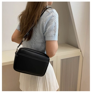 Detail view of black leather crossbody camera bag with contrast white stitching and strap