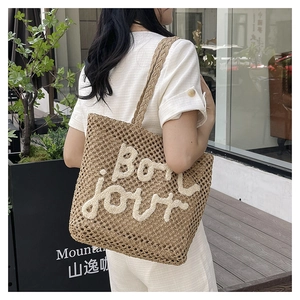 Detailed view of woven straw tote bag featuring Bonjour embroidery in a casual outdoor setting