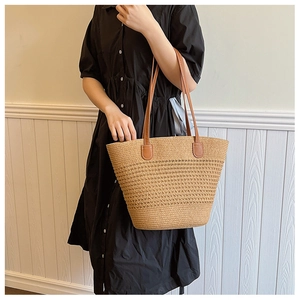 Detail of woven straw texture and premium brown leather handle on a large summer tote bag