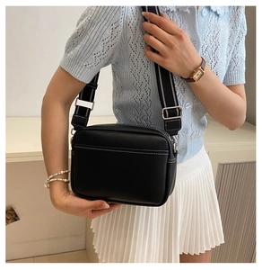 Minimalist black leather camera bag with white stitching and striped canvas strap