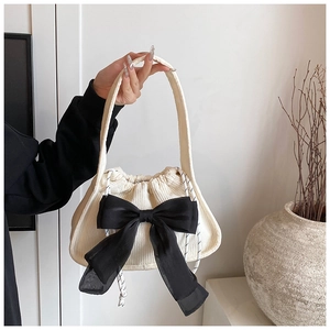 Close-up of cream corduroy handbag with a large black chiffon bow and drawstring detail