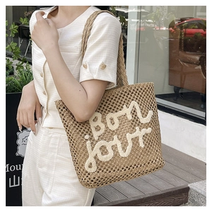 Detail showing woven texture and white bouclé 'bon jour' embroidery on khaki straw tote bag