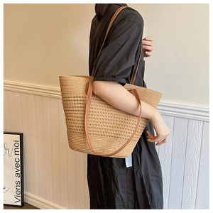 Detail of hand-woven straw tote bag with brown leather straps worn by a model
