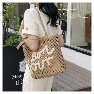 Detail view of woven straw tote bag featuring white bouclé embroidered Bon Jour text