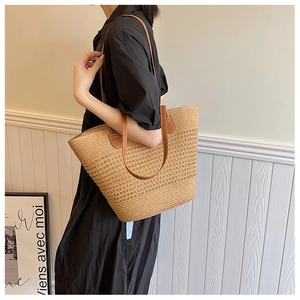 Macro view of woven straw tote bag with brown leather handles on a model in a minimalist room