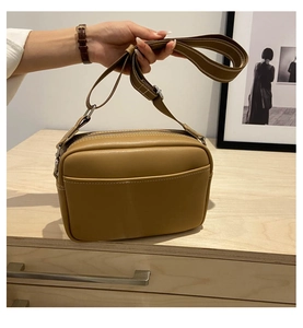 Detail view of brown faux leather camera bag with wide fabric strap on wooden cabinet
