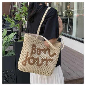 Detail of a beige woven straw tote bag featuring brown fuzzy Bonjour text embroidery