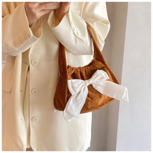 Detail of a brown corduroy handbag with a large white satin bow held by a model