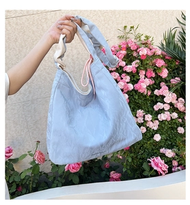 Close-up of light blue pleated PU handbag with fashion branding and beige strap detail