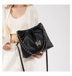 Detail of black pleated bucket bag with silver butterfly buckle and gold chain strap