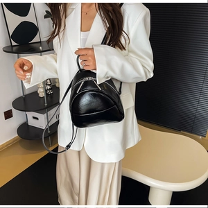 Minimalist black glossy PU leather mini backpack shown on a model in a modern indoor setting