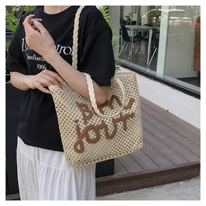 Detail of off-white woven straw tote bag with brown Bon Jour embroidery and braided handle