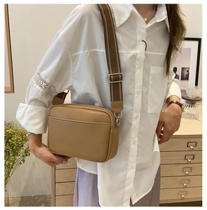 Detail view of khaki PU leather camera bag with wide canvas strap on model in cozy interior