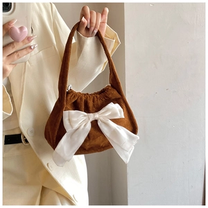 Detailed texture of brown corduroy fabric with large white satin bow on small handbag