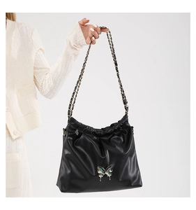 Detail of black pleated PU leather shoulder bag with a colorful butterfly metal accent