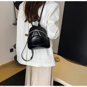 Chic black mini PU leather backpack shown on a model with white blazer in a minimalist setting