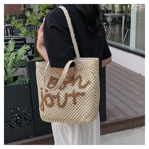 Detail of hand-woven straw tote bag featuring embroidered bon jour text and long shoulder straps