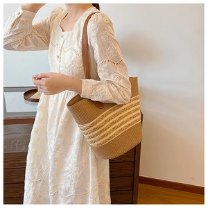 Detail of woven straw tote bag with brown leather strap and beige stripes
