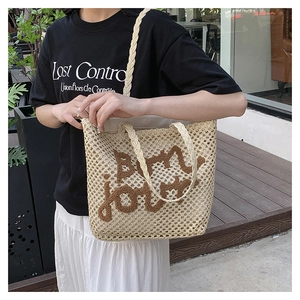 Detail of hand-woven beige straw tote bag with brown embroidered Bonjour lettering