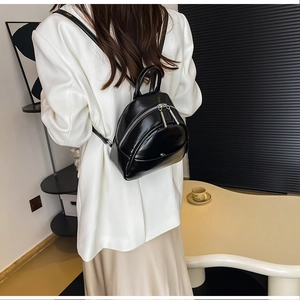 Rear view of a black mini PU leather backpack with silver zippers on a fashion model