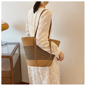 Detail of woven straw tote bag with black stripes and brown leather strap on model
