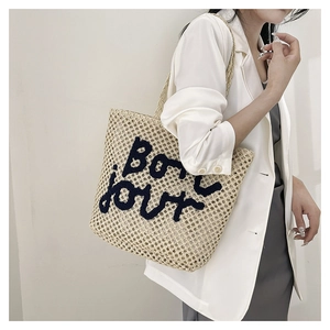 Detail of woven straw tote bag featuring Bonjour embroidery and mesh texture