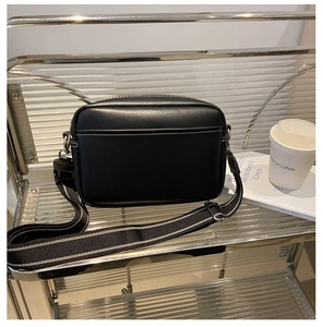 Detail of black camera bag featuring white contrast stitching and striped fabric strap