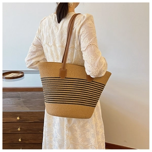 Detail of woven straw tote bag with black stripes and brown leather shoulder straps