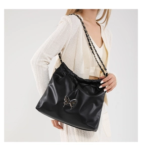 Detail of black bucket bag with silver butterfly charm and chain strap on shoulder