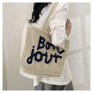 Detail of beige woven tote bag with Bonjour embroidery shown in soft natural sunlight