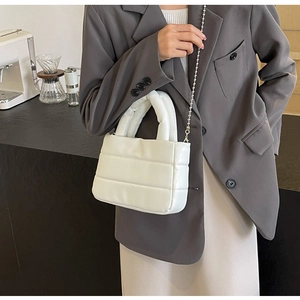 Detail of white quilted puffy handbag with silver ball chain strap on a model