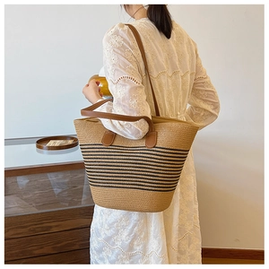 Detail view of woven straw tote bag featuring brown leather straps and black stripe accents