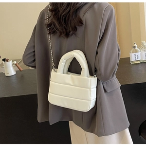 Detail of white quilted crossbody bag with metal chain strap and puffy texture design