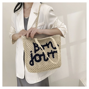 Detail of woven straw tote bag featuring black embroidered Bon jour French lettering