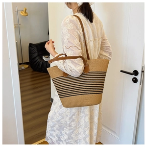 Detailed view of woven straw tote bag with black stripes and brown leather straps