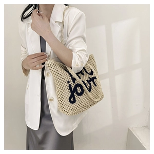 Detail of beige woven straw tote bag with black jour embroidery and handle