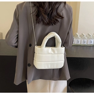 Detail of white puffer crossbody bag with quilted texture and silver bead chain strap