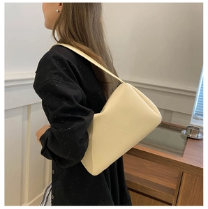 Close-up of cream-colored shoulder bag with litchi texture on a model in minimalist setting